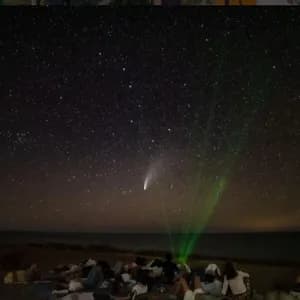 Un viaggio di gruppo WeRoad per osservare le stelle e una cometa su una spiaggia di notte, sotto un cielo stellato.