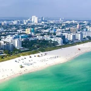 Vue aérienne d'un paysage urbain moderne avec des gratte-ciel, longeant une large plage de sable blanc et des eaux océaniques turquoise.