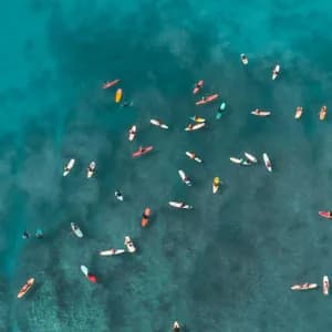 Una vista aérea de un viaje en grupo de WeRoad en tablas de surf y kayaks dispersos en aguas claras y turquesas.