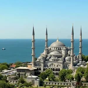 A large mosque with multiple domes and six minarets overlooking a sea filled with ships under a clear blue sky.