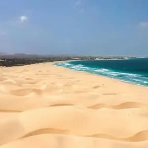 Vastas dunas de arena dorada descienden hasta el encuentro de las olas turquesas del océano a lo largo de una extensa costa.