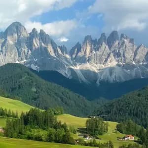 Un petit village avec son église, niché dans une vallée verdoyante au pied de collines boisées et d'une chaîne de montagnes rocheuses et déchiquetées.