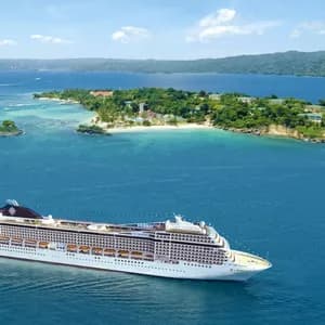 Una grande nave da crociera bianca naviga sull'oceano blu, passando accanto a un'isola tropicale lussureggiante e verde.