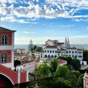 A view over a historic town with colorful buildings, including a palace with two large conical chimneys, under a blue cloudy sky.