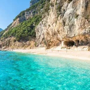 Acque turchesi lambiscono una spiaggia sabbiosa e appartata ai piedi di un'imponente scogliera frastagliata sotto un cielo limpido.