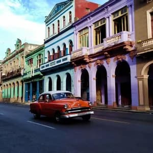 Un coche vintage naranja circula por una calle junto a coloridos edificios coloniales con puertas arqueadas bajo un cielo azul.