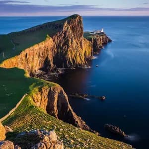 Un faro blanco se asienta en una península rocosa y cubierta de hierba que se adentra en el tranquilo mar azul, iluminado por la cálida luz del atardecer.