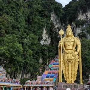 Une grande statue dorée d'une divinité se dresse à côté d'un escalier arc-en-ciel coloré qui monte le long d'une falaise luxuriante couverte de jungle.