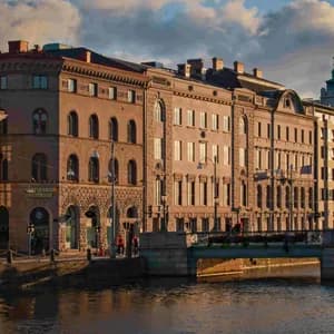 Sunlight during the golden hour illuminates ornate buildings lining a city canal, with reflections in the water.