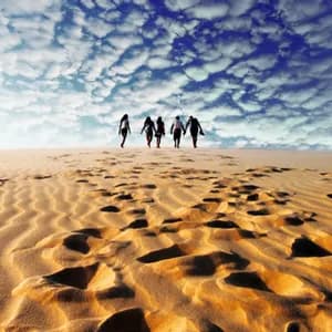 Un voyage de groupe WeRoad traverse une vaste dune de sable, laissant des empreintes dans le sable sous un ciel bleu nuageux.
