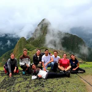 Un viaje en grupo de WeRoad posa para una foto en un mirador cubierto de hierba, con montañas cubiertas de niebla al fondo.