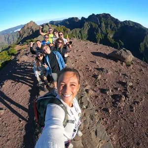 Un voyage en groupe WeRoad sourit pour un selfie sur une crête rocheuse de montagne avec des sommets en arrière-plan.