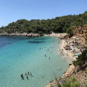 Una vista dall'alto di una caletta affollata con persone che nuotano in acqua limpida e turchese e prendono il sole sulla sabbia.