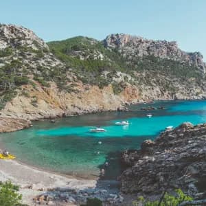 Eine Luftaufnahme einer abgelegenen Bucht mit klarem türkisfarbenem Wasser, wo mehrere Boote nahe einem Kieselstrand ankern.