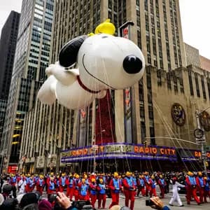 Un grande pallone di Snoopy fluttua sopra una parata in una strada cittadina di fronte alla Radio City Music Hall, con la folla che osserva.