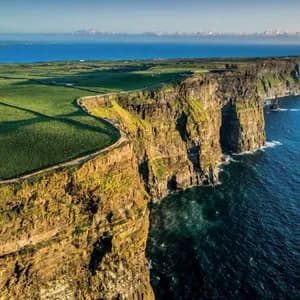 Vista aerea di ampie scogliere verdi lungo una costa, con acqua oceanica di un blu profondo sotto un cielo sereno.