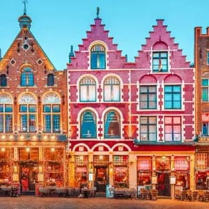 Una hilera de casas de colores, tradicionales y con tejados a dos aguas, decoradas con luces y árboles de Navidad en una plaza adoquinada al anochecer.