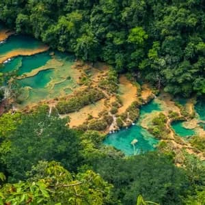 Una veduta aerea di piscine naturali a terrazze con acqua turchese che scorre attraverso una fitta giungla verde e lussureggiante.