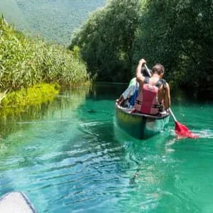 Un viaggio di gruppo WeRoad pagaia in canoa lungo un fiume limpido e turchese, fiancheggiato da alte canne verdi e alberi.