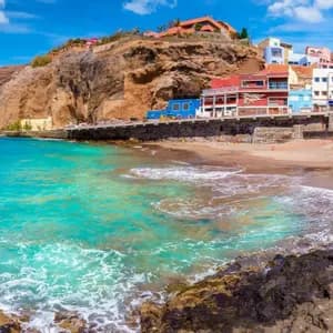 Ein Panoramablick auf ein Küstendorf mit bunten Gebäuden an einer Klippe neben einem Strand mit türkisfarbenem Wasser.