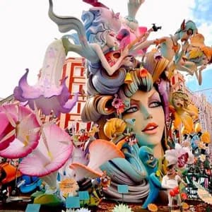 Una scultura imponente e colorata, raffigurante un grande volto femminile, figure fantastiche e fiori, si erge all'aperto in una città.