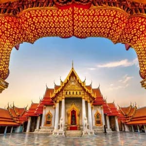 Un templo tailandés tradicional con techos dorados y paredes de mármol blanco, visto a través de un arco ornamentado, decorativo, dorado y rojo.