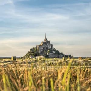 Eine historische Burg auf einem felsigen Hügel, gesehen über ein Feld voller hohem Gras und Heuballen im Sonnenuntergang.