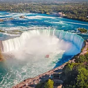 Veduta aerea di una massiccia cascata a ferro di cavallo con una barca turistica che naviga le acque nebbiose alla sua base.
