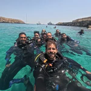 Un gruppo WeRoad in viaggio si scatta un selfie, completamente equipaggiato da sub, mentre galleggia insieme in acque limpide e turchesi.