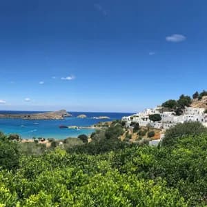 Un villaggio imbiancato a calce e un'acropoli su un pendio che domina una baia turchese, con alberi verdi in primo piano.