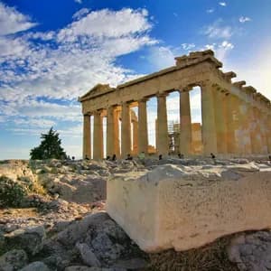 Un antiguo templo griego con grandes columnas se alza sobre una colina rocosa bajo un cielo azul con nubes blancas al atardecer.