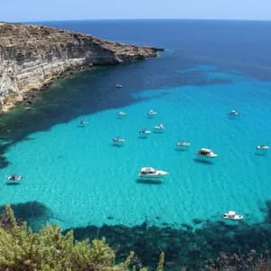 Veduta dall'alto di diverse imbarcazioni che galleggiano su acque turchesi in una baia vicino a ripide scogliere rocciose.