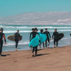 Un gruppo WeRoad di surfisti in muta con le loro tavole cammina lungo una spiaggia sabbiosa verso le onde dell'oceano.