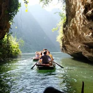 Un viaje en grupo de WeRoad rema en botes por un río a través de un desfiladero soleado entre grandes acantilados rocosos.