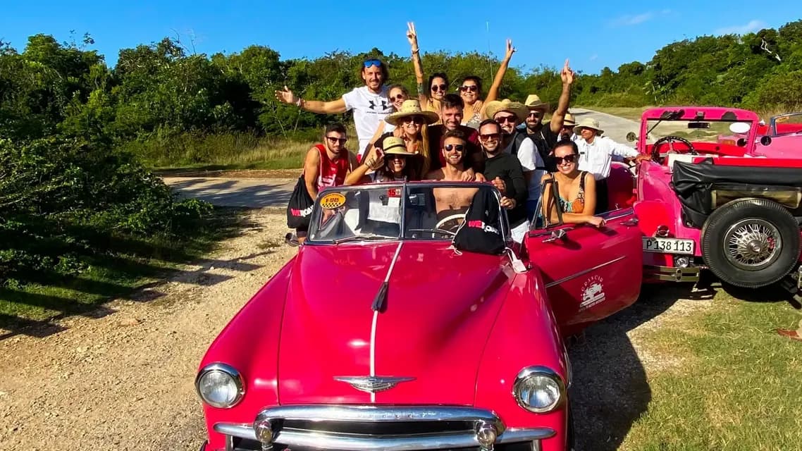 Eine WeRoad-Gruppenreise posiert für ein Foto in zwei leuchtend pinken Vintage-Cabrios an einem sonnigen Tag.