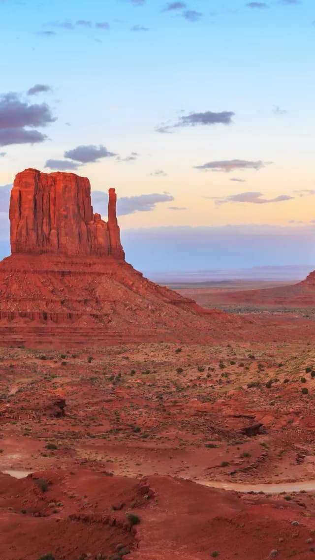Un imponente picco di arenaria rossa si erge dal deserto sotto un cielo di nuvole soffici al crepuscolo.