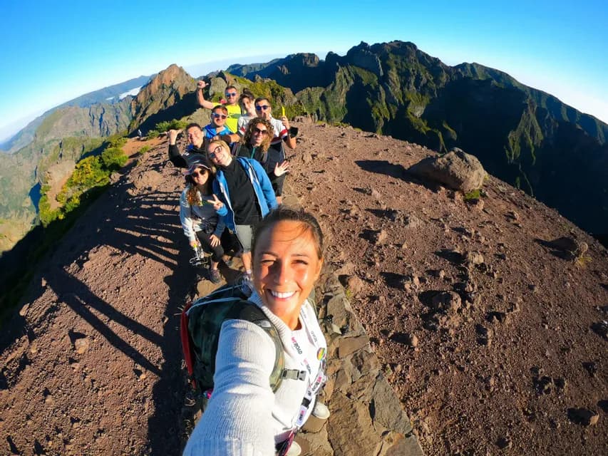 Un gruppo WeRoad si fa un selfie mentre fa trekking su uno stretto crinale di montagna roccioso sotto un cielo azzurro e limpido.