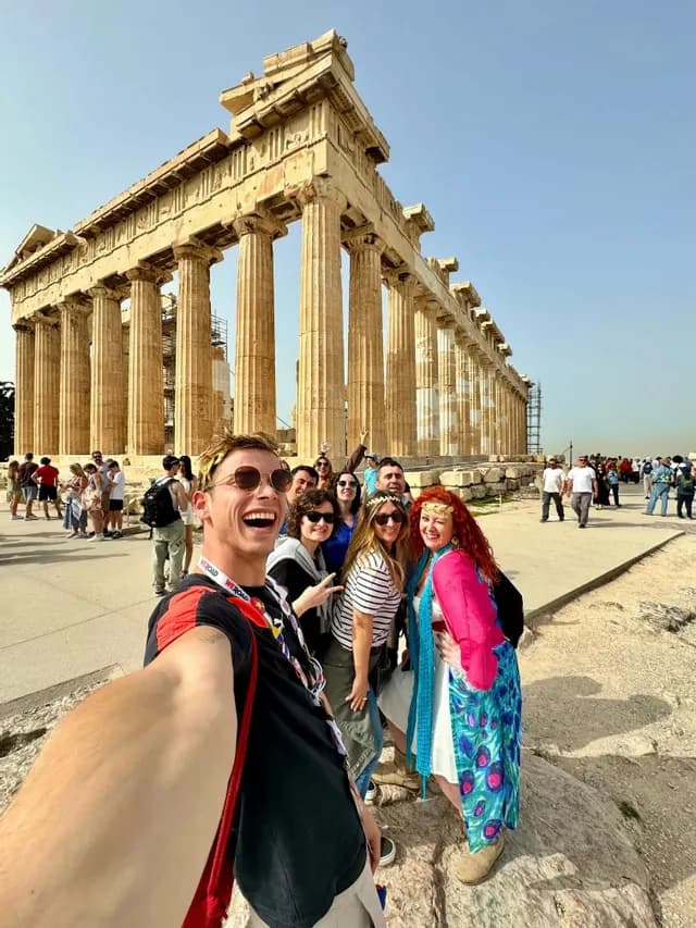 Un viaje en grupo de WeRoad se toma una selfie sonriente frente a un templo grande y antiguo con columnas.