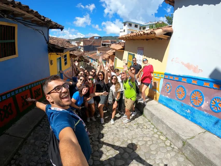 Un hombre se toma una selfie gran angular con su grupo de WeRoad durante un viaje, en una calle adoquinada y estrecha, con edificios coloridos.