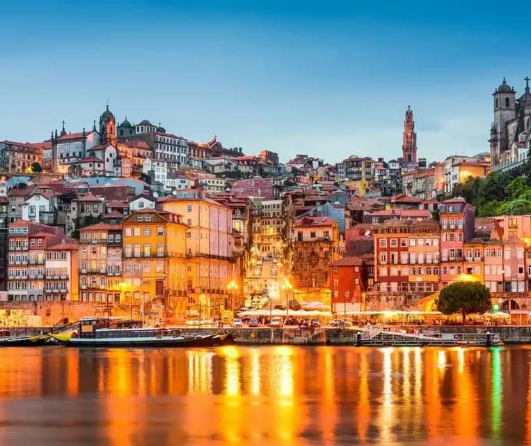 Un paesaggio urbano collinare colorato illuminato al crepuscolo, con le luci degli edifici che si riflettono sul fiume calmo sottostante.