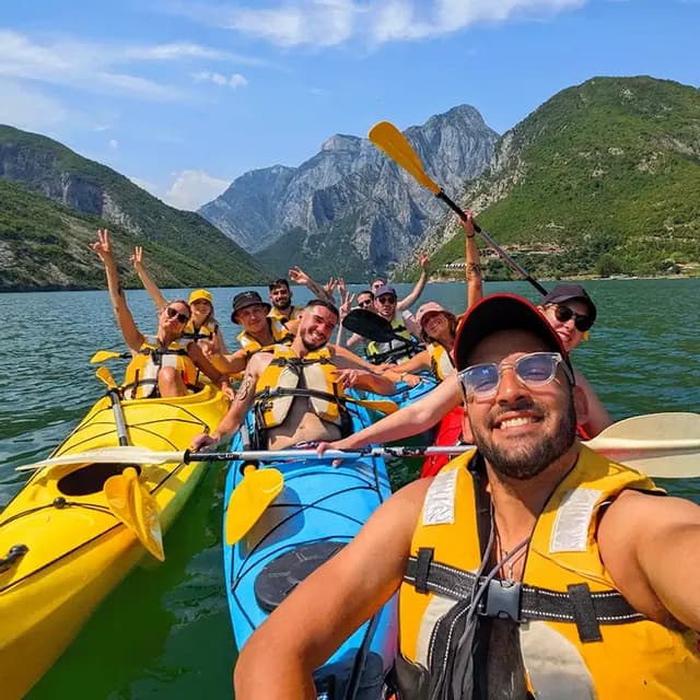 WeRoad-Gruppenreise: Lächelnde Menschen machen ein Selfie beim Kajakfahren auf einem See mit Bergen im Hintergrund.