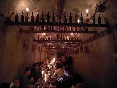 Un grupo de WeRoad cena en una bodega rústica e iluminada con velas, con botellas de vino dispuestas en estantes.