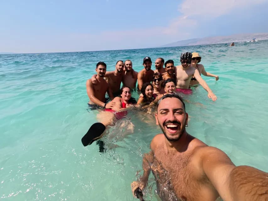 Eine WeRoad-Gruppenreise macht ein lächelndes Selfie, während sie gemeinsam im klaren türkisfarbenen Wasser unter blauem Himmel schwimmen.