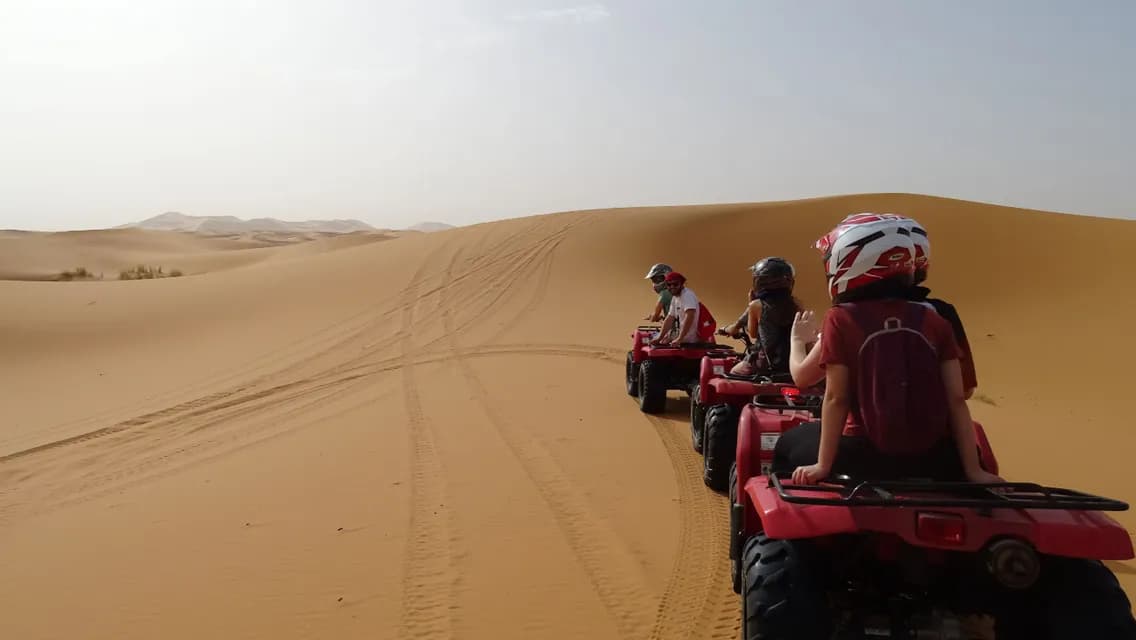 Un voyage de groupe WeRoad à bord de quads rouges, traversant en ligne de vastes dunes de sable dans le désert.