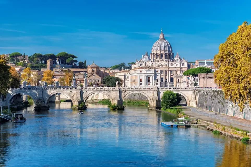Una vista de la Basílica de San Pedro y el Puente Sant'Angelo sobre un río ancho bajo un cielo azul claro.