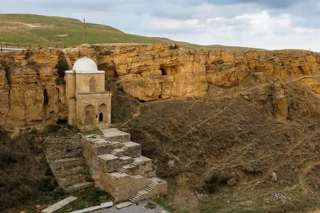 Un mausoleo di pietra con cupola bianca incastonato in una scogliera rocciosa, con ampie piattaforme e gradini in pietra in primo piano.