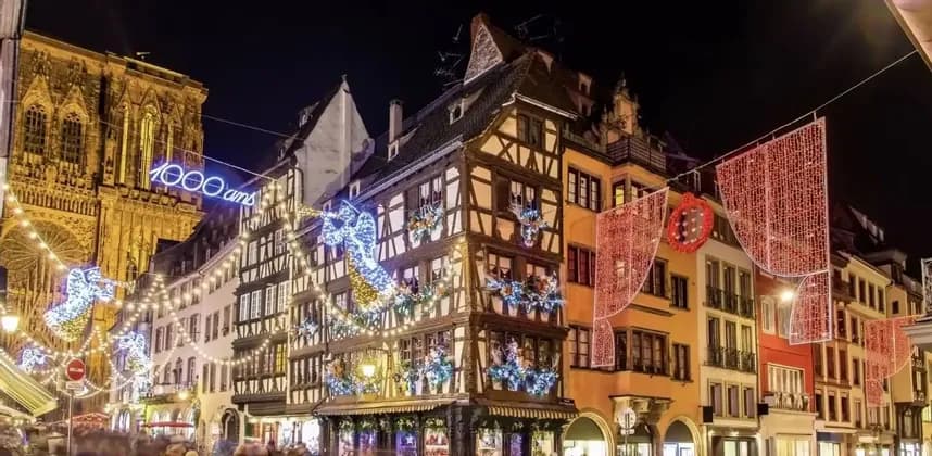 Una calle histórica con edificios de entramado de madera y una catedral decorada con luces y adornos navideños brillantes por la noche.
