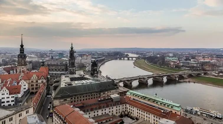 An aerial view of a historic European city with a wide river, several stone bridges, and ornate architecture under a cloudy sky.