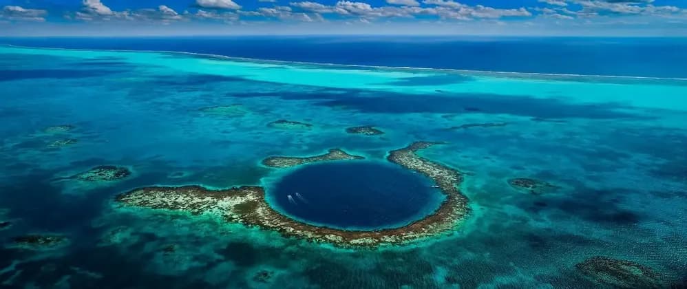 Luftaufnahme eines großen blauen Lochs, umgeben von einem Korallenriff in türkisfarbenem Wasser, mit zwei kleinen Booten, die darin fahren.
