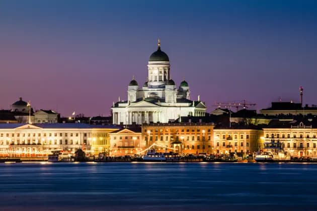 La Cattedrale illuminata di Helsinki e i palazzi sul lungomare della città, visti dall'acqua al crepuscolo.